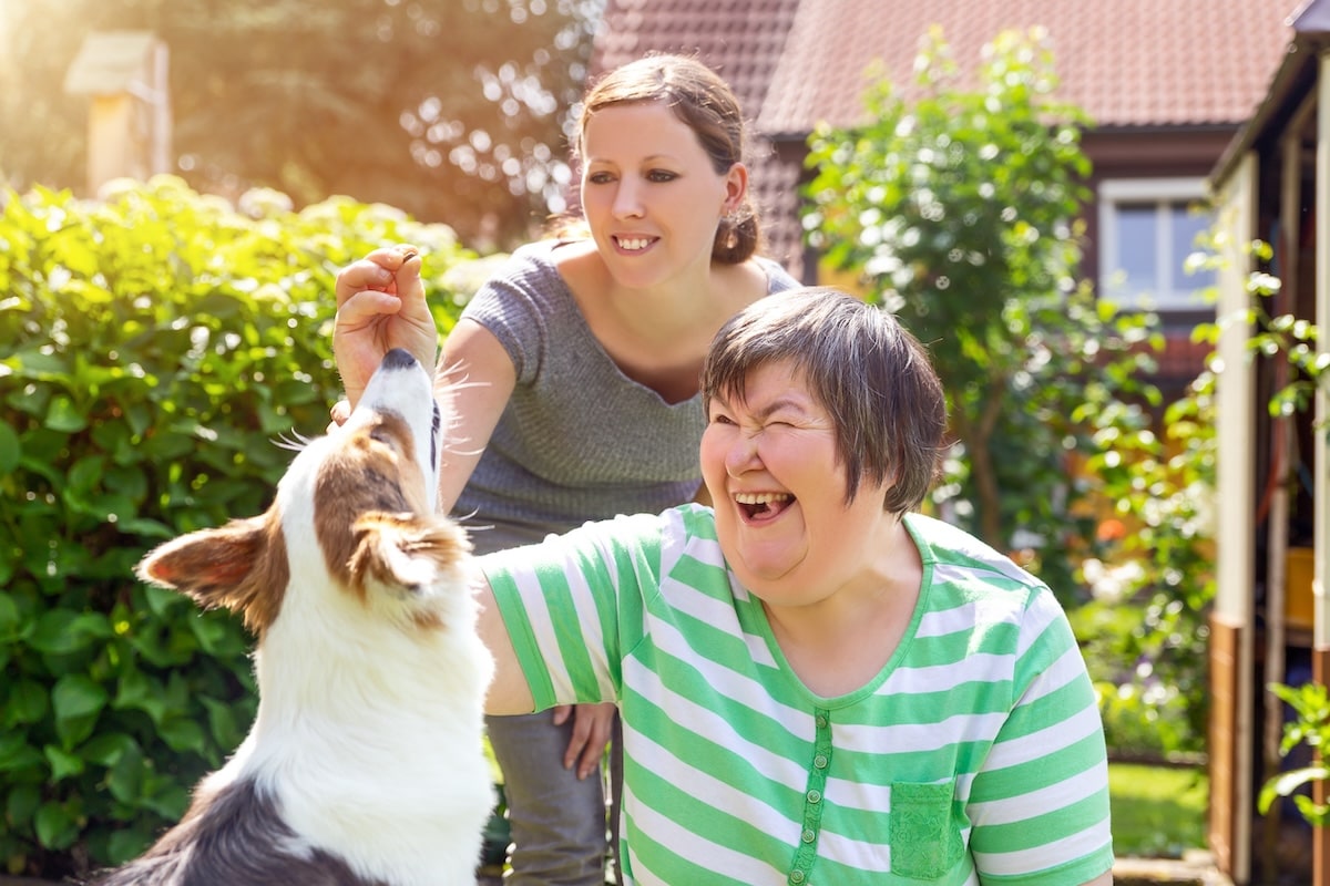 A woman helping a disabled woman feed a treat to a dog